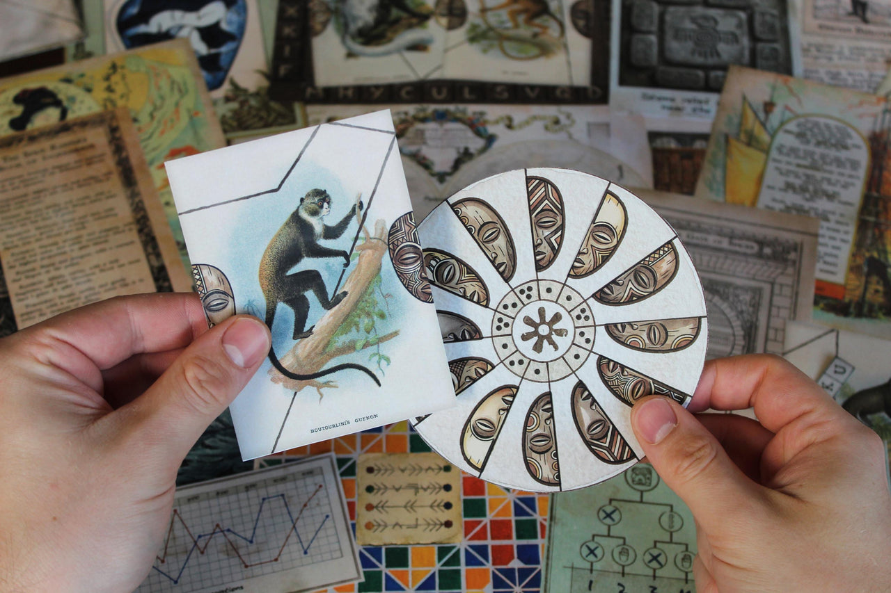 Hands-on African-themed puzzle from Expedition Around the World printable escape room, showing a player holding a vintage monkey illustration and rotating cipher disk decorated with African masks. Other travel puzzle materials, maps, coded diagrams, Moroccan mosaic tiles, journal pages, and ancient symbols appear in the background. This DIY escape room for adults uses interactive paper components, pattern matching, decoding, logic, and observation across a globe-spanning mystery adventure.